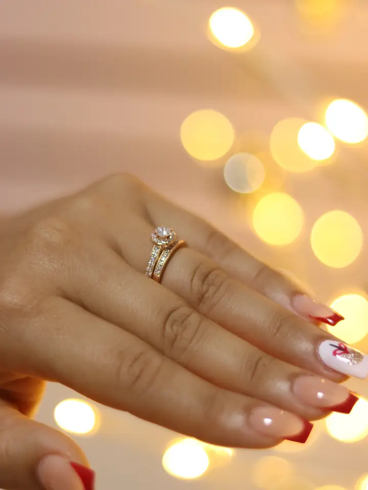 Polished nails and a diamond ring against warm bokeh light