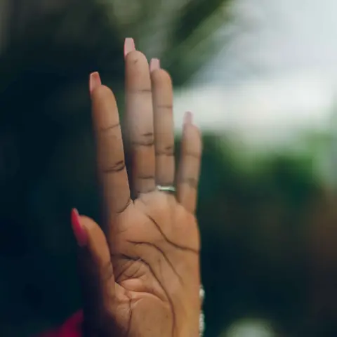 Hand with long pink nails resting on a glass